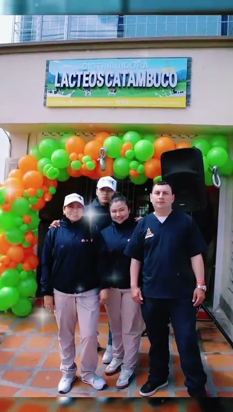 Equipo de Lácteos Catambuco frente al punto de atención, bajo el aviso de la marca y un arco de globos naranjas y verdes
