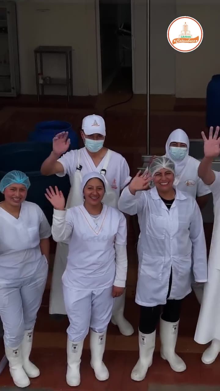 Trabajadoras de Lácteos Catambuco con uniforme blanco y cofia saludando dentro de la planta