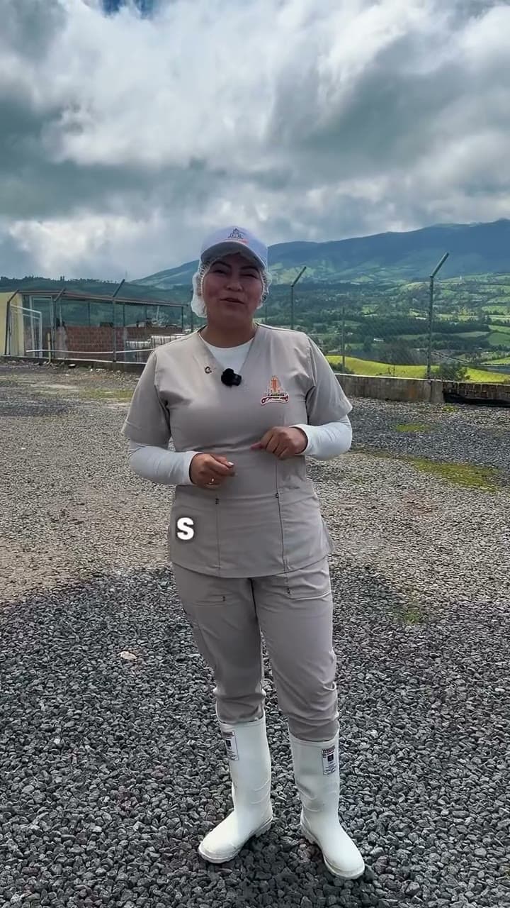 Trabajadora de Lácteos Catambuco con uniforme y cofia frente a la planta, con las montañas de Nariño al fondo